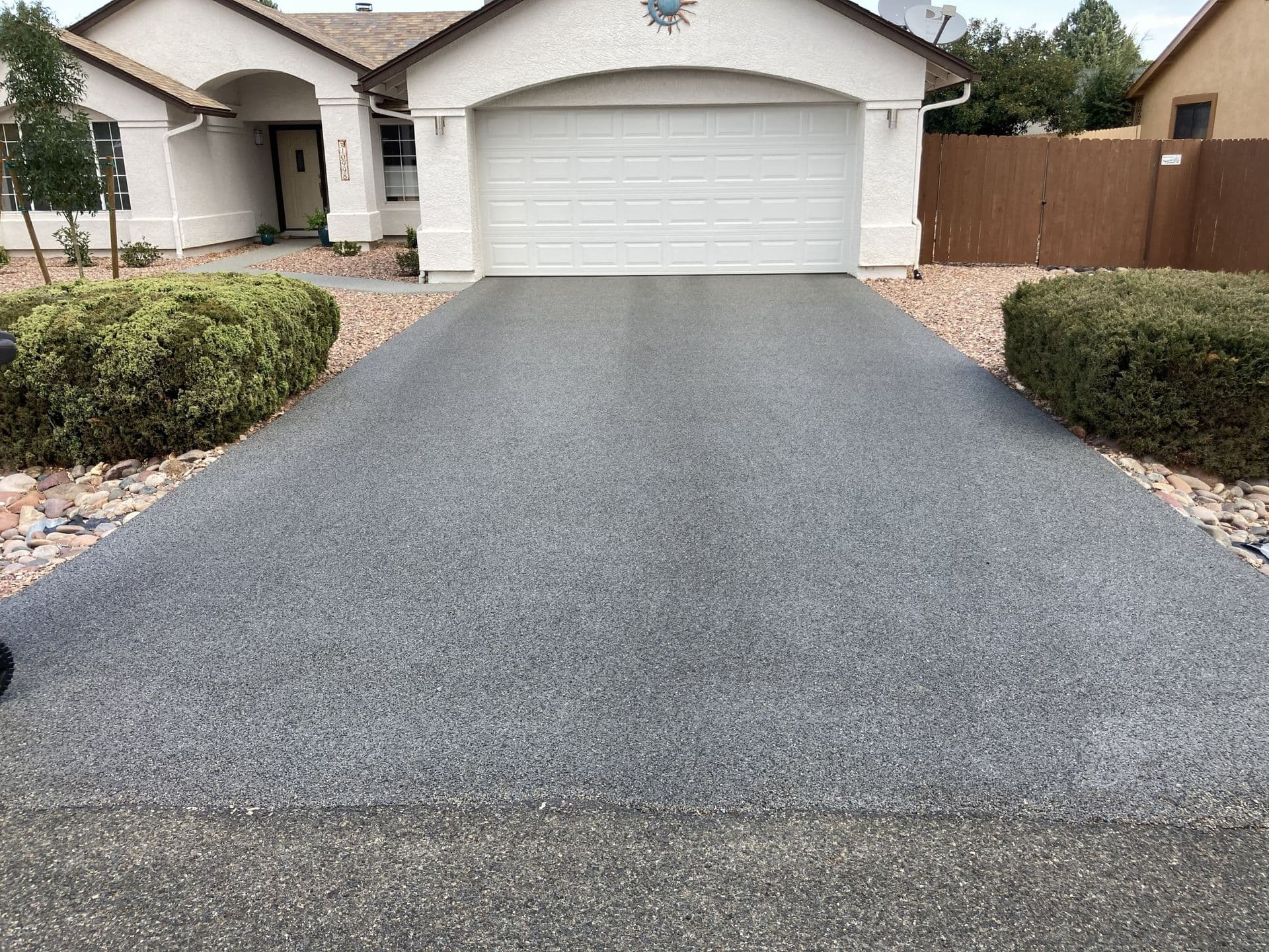 A newly-paved gray driveway in front of a white stucco house.