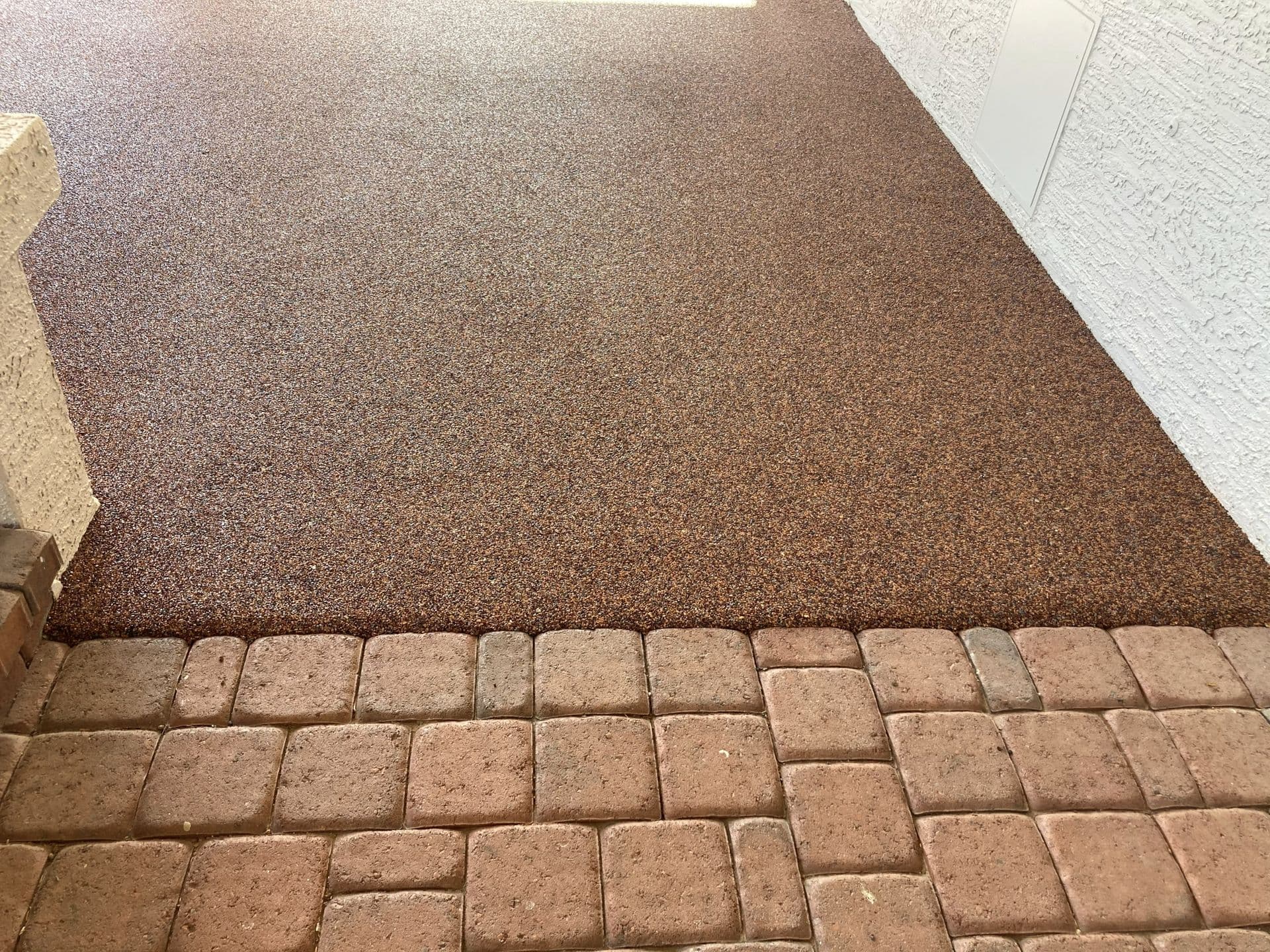 A brown speckled rubber stone walkway abuts tan paver stones.